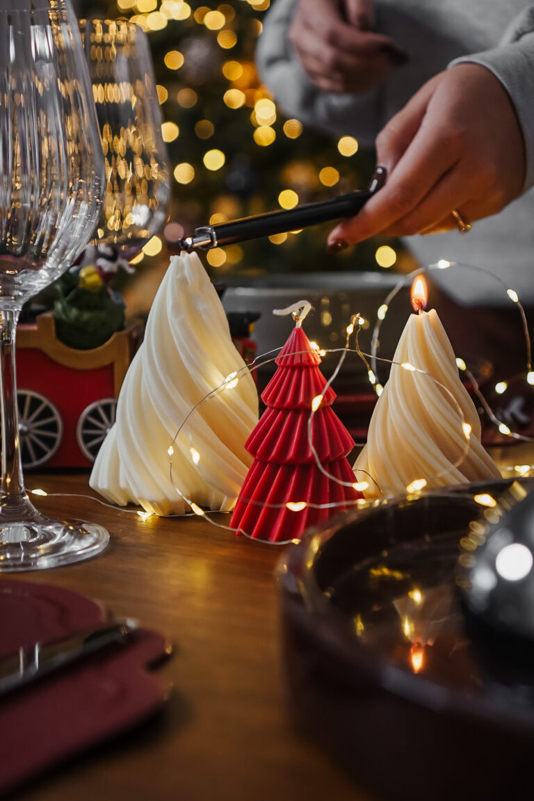 Main allumant une bougie sapin torsadé blanc à côté d’une bougie sapin rouge