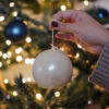 Bougie blanche en forme de boule de Noël tenue à la main devant un sapin décoré