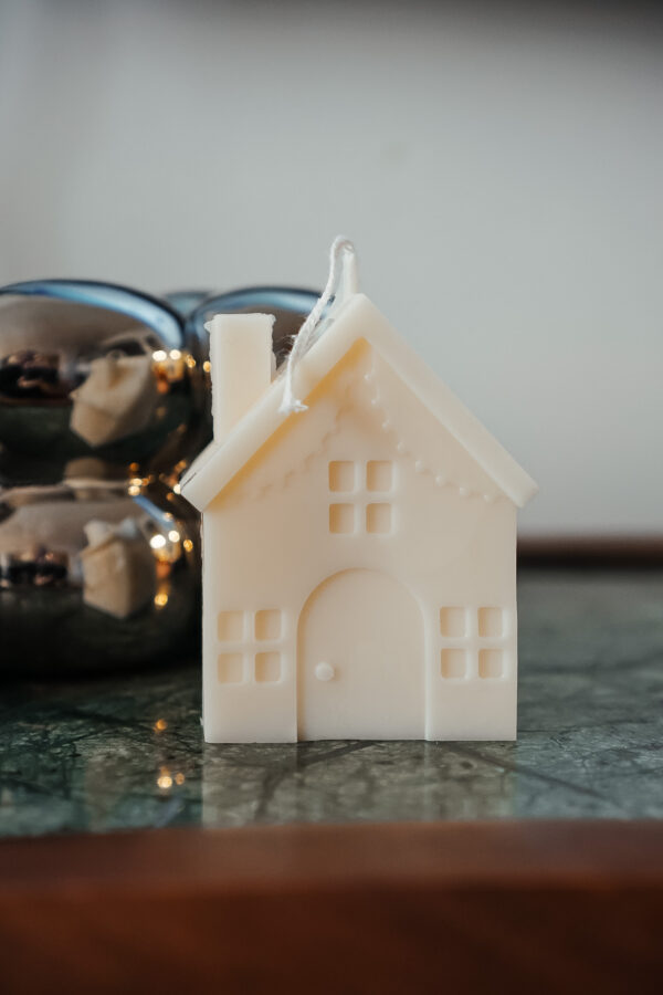 Bougie décorative blanche en forme de maison, sur fond festif, fabriquée artisanalement en Belgique