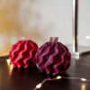 Bougies Boule Torsadee Ysadena Rouge et Violet Bougies sculpturales torsadées rouges et violettes Ysadena posées sur un meuble