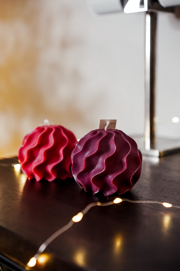 Bougies Boule Torsadee Ysadena Rouge et Violet Bougies sculpturales torsadées rouges et violettes Ysadena posées sur un meuble