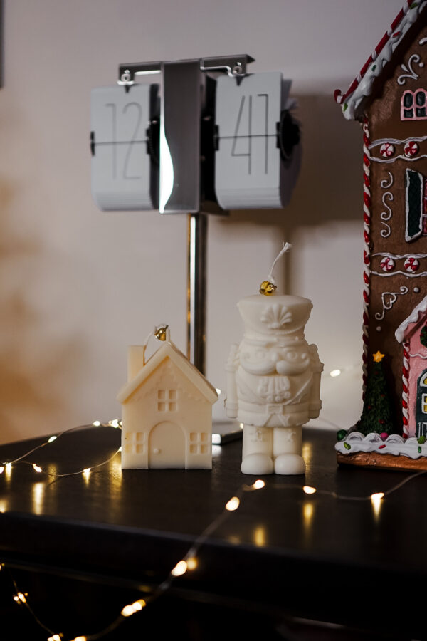 Bougies sculpturales Maison d’Hiver et Casse-Noisette posées sur un meuble avec guirlande lumineuse